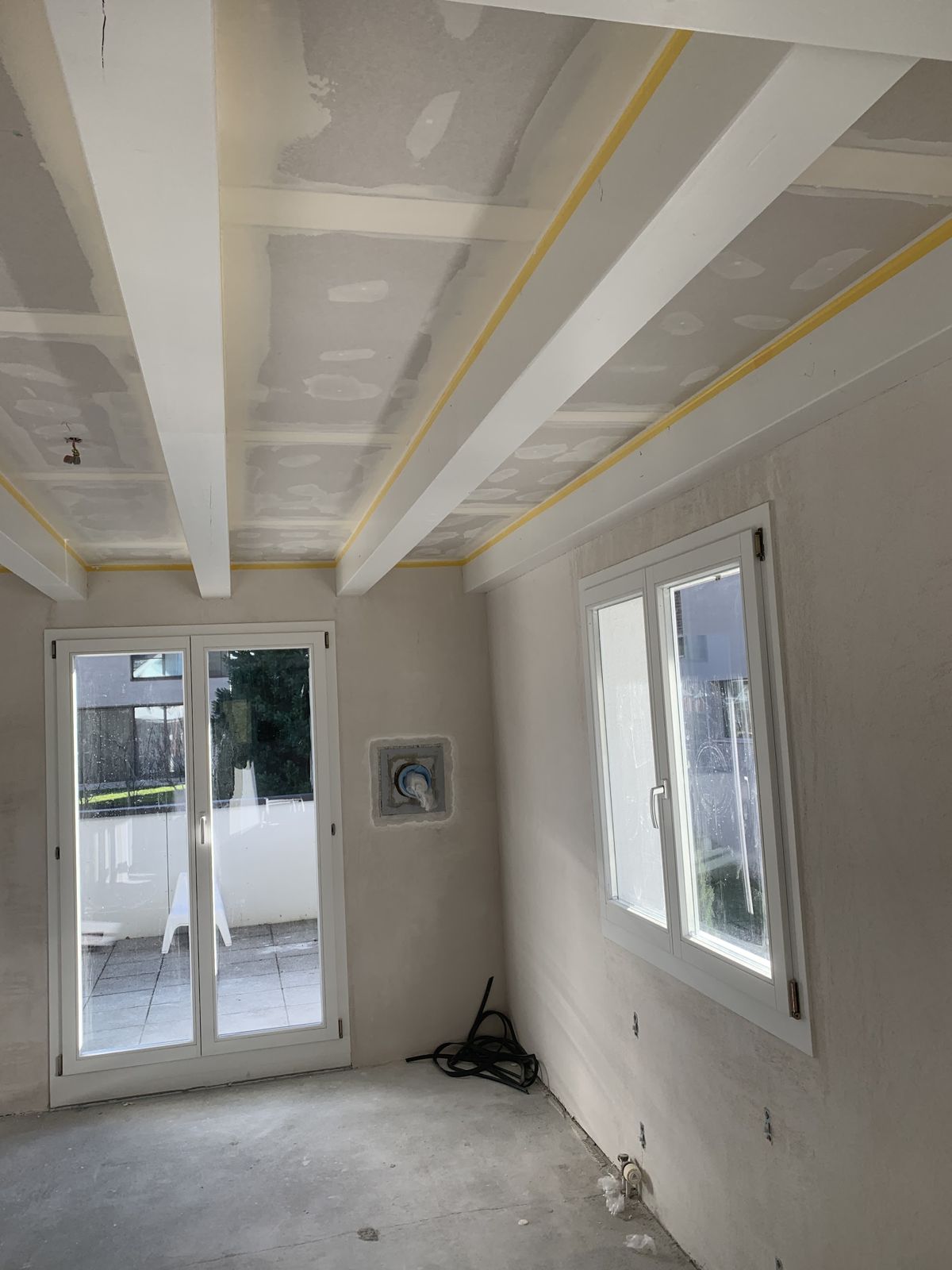 Renovierter Raum mit weissen Deckenbalken und Fenstertür